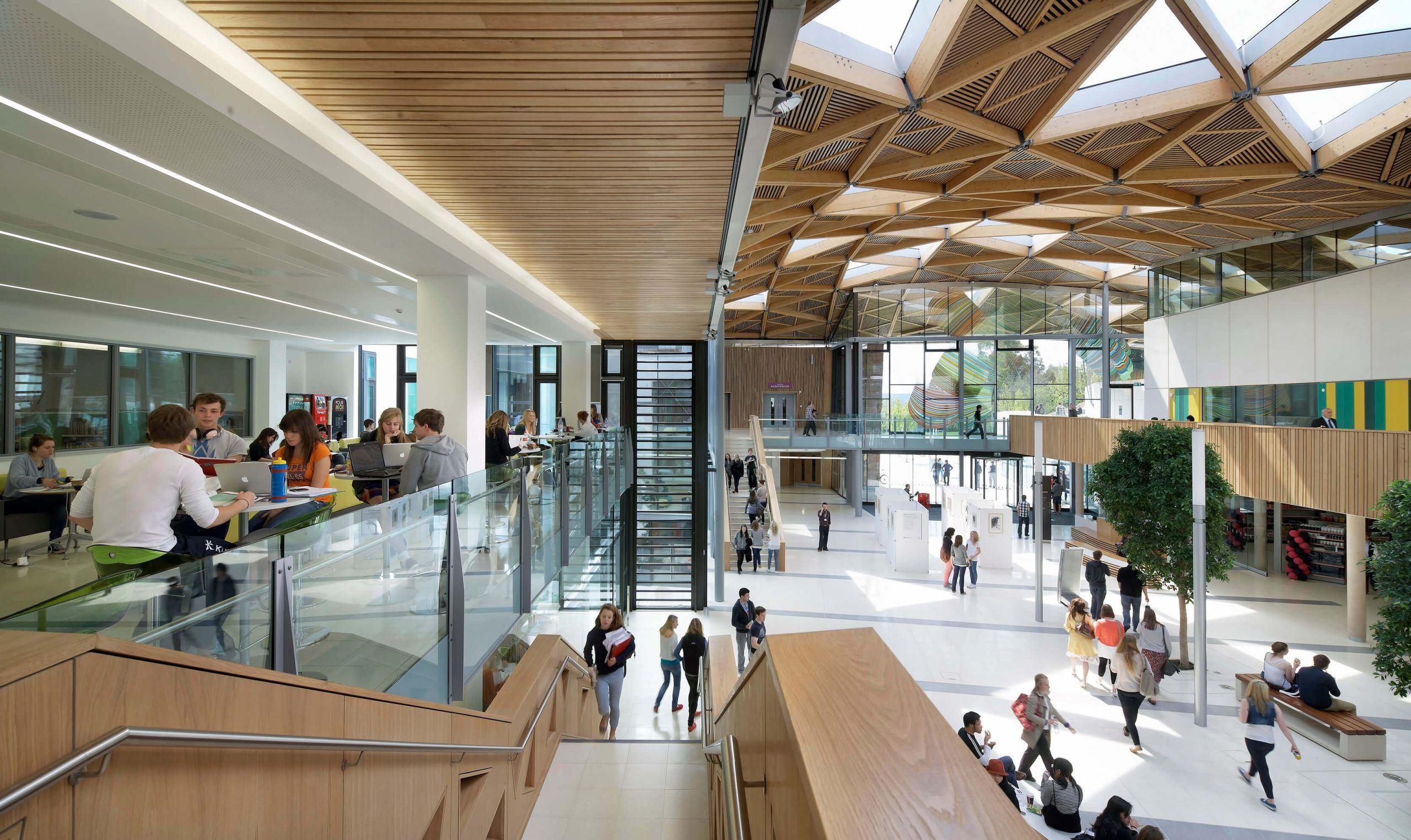 People working and walking in a bright atrium with a wooden ceiling and glass railings